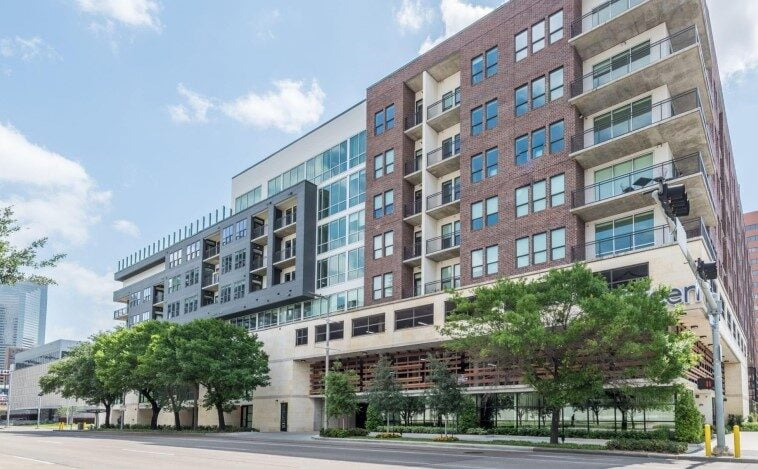 Street-level view of Eighteen25 Downtown Apartments with green trees lining the front."